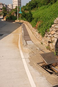 馬祖酒廠往復興村路口,石頭路標旁陰井蓋翹起;鄉公所表示,已將此處陰井與水溝納入聯勤睦鄰經費改善。(圖/文:邱竟瑋)