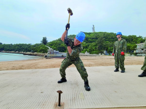 官兵以長鋼釘將戰術機動蓆固定沙灘上。（圖：程婉琳）