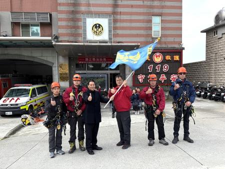 縣長王忠銘為即將赴台參與「繩期繩索救援國際邀請賽」的消防及義消同仁授旗並致贈加菜金，期勉為縣爭光、平安完賽。（圖／文：王致潔）