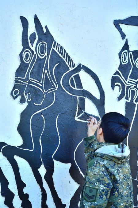 西引島「200商店」對面，身著現代迷彩服的官兵正全神貫注地為牆面浮雕漆上新色。「新舊同框」的畫面，呈現了國軍跨越半世紀的戰地傳承，讓古老的軍事圖騰在現代營區中重新煥發生命力。（圖／文：陳其敏）