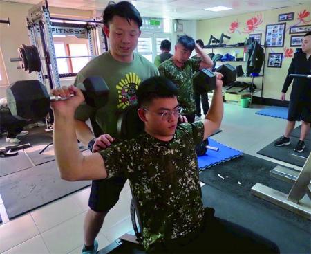 康教官輔助官兵正確操作器材，加強二頭肌訓練。