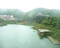 勝利水庫雨中即景,遠方民俗文物館前有流水不斷挹注,浮現已久的「乾旱指標」也漸漸沒入水中。(圖/文:曹重偉)