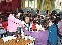 　「春之鍊」串起陣陣思念，指導老師曹立淇親切的幫學員將剛完成的作品戴在手腕上。（圖／文：曹重偉）