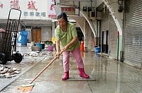介壽商場住戶表示,只要下起大雨渾濁的黃水就會淹到家裡面,圖中的住戶在雨勢稍歇的時候,穿著雨鞋正在用掃把做清理工作。(圖/文:張登傑)
